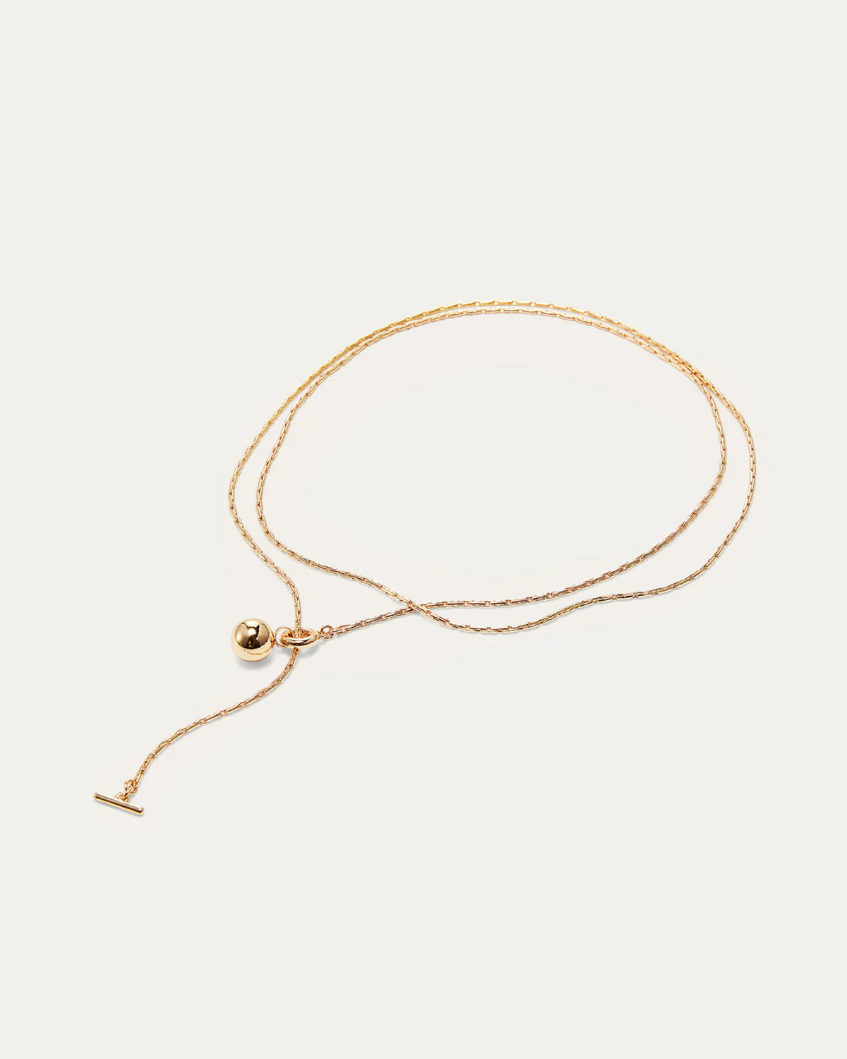 Gold necklace with a small pendant on a light beige background