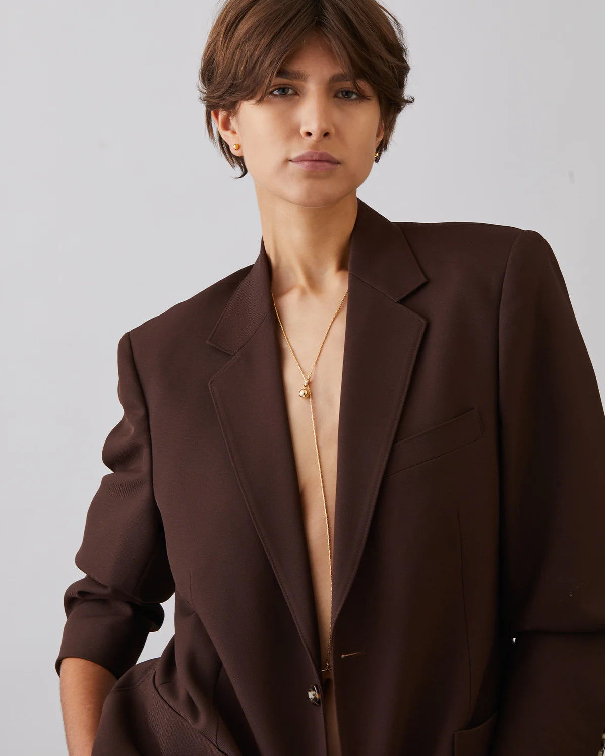 Woman wearing a brown blazer over a beige top against a plain background
