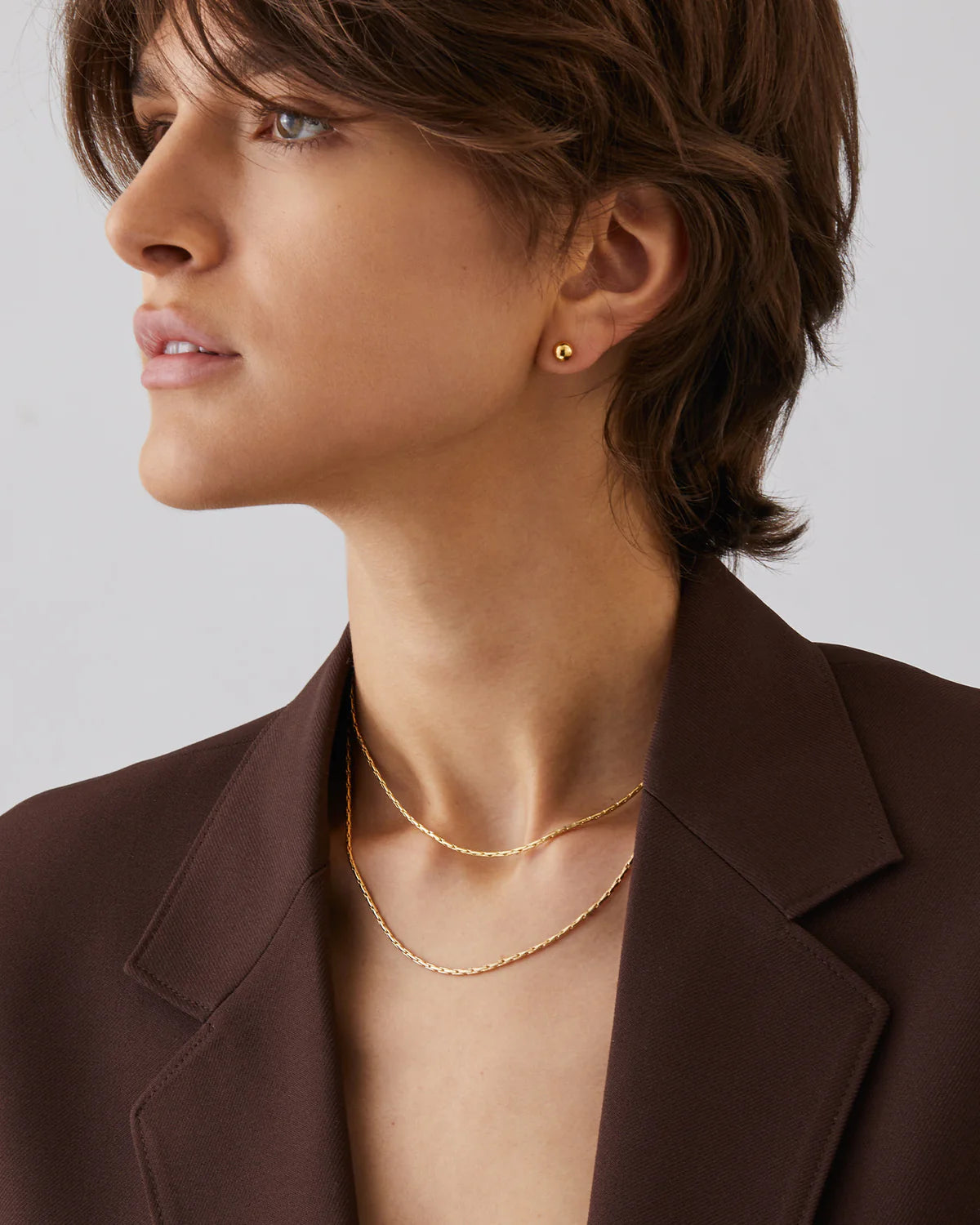 Woman wearing gold earrings and necklace against a neutral background