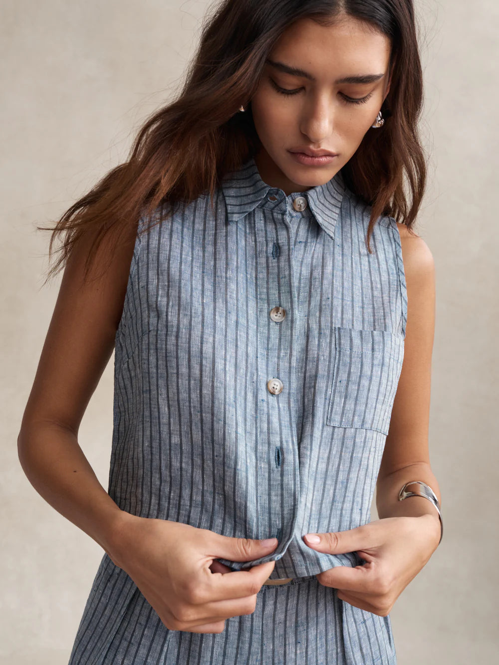 Woman wearing a sleeveless blue striped shirt against a beige background