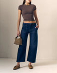 model waring blue jeans with a short sleeve brown top holding a woven bag on a cream background 