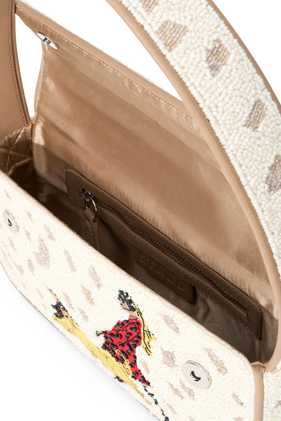 Close-up of a handbag interior and upper flap, showing a beige satin-lined compartment, brown zipper, and a cream patterned exterior with a small embroidered figure in red and yellow.