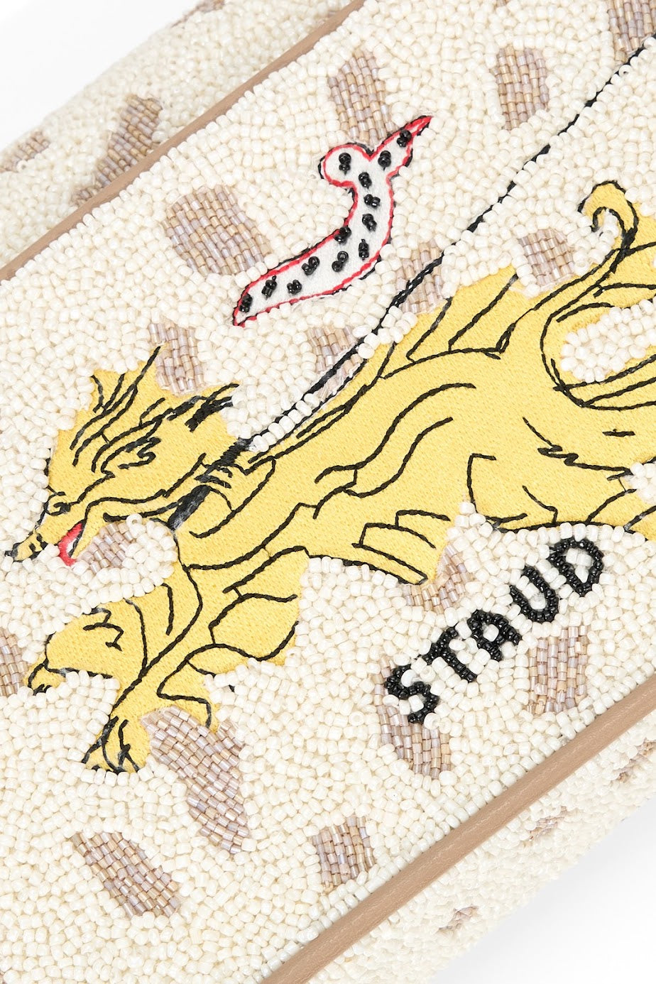 Close-up of a textured cream beaded fabric featuring a yellow embroidered dragon, a red-and-black spotted snake, and the word 'STAUD' in black beads.
