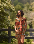 A woman wearing a bohemian-style two-piece matching set with a tie-front scarf, standing outdoors in a grassy park with trees and a fence in the background.