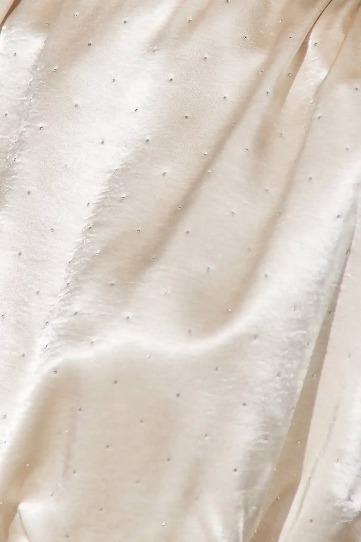 A close-up of draped cream satin fabric with a subtle dotted pattern of small metallic studs.