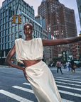 A model wearing a shimmering cream satin two-piece set consisting of a cropped puff-sleeve top and a matching high-waisted skirt, posing on a city crosswalk with skyscrapers in the background.