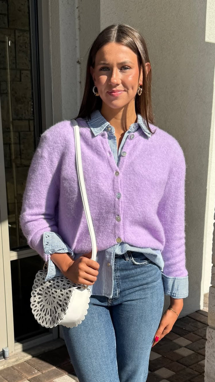 Woman wearing a light purple cardigan over a denim shirt, holding a white handbag.