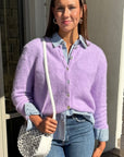 Woman wearing a light purple cardigan over a denim shirt, holding a white handbag.