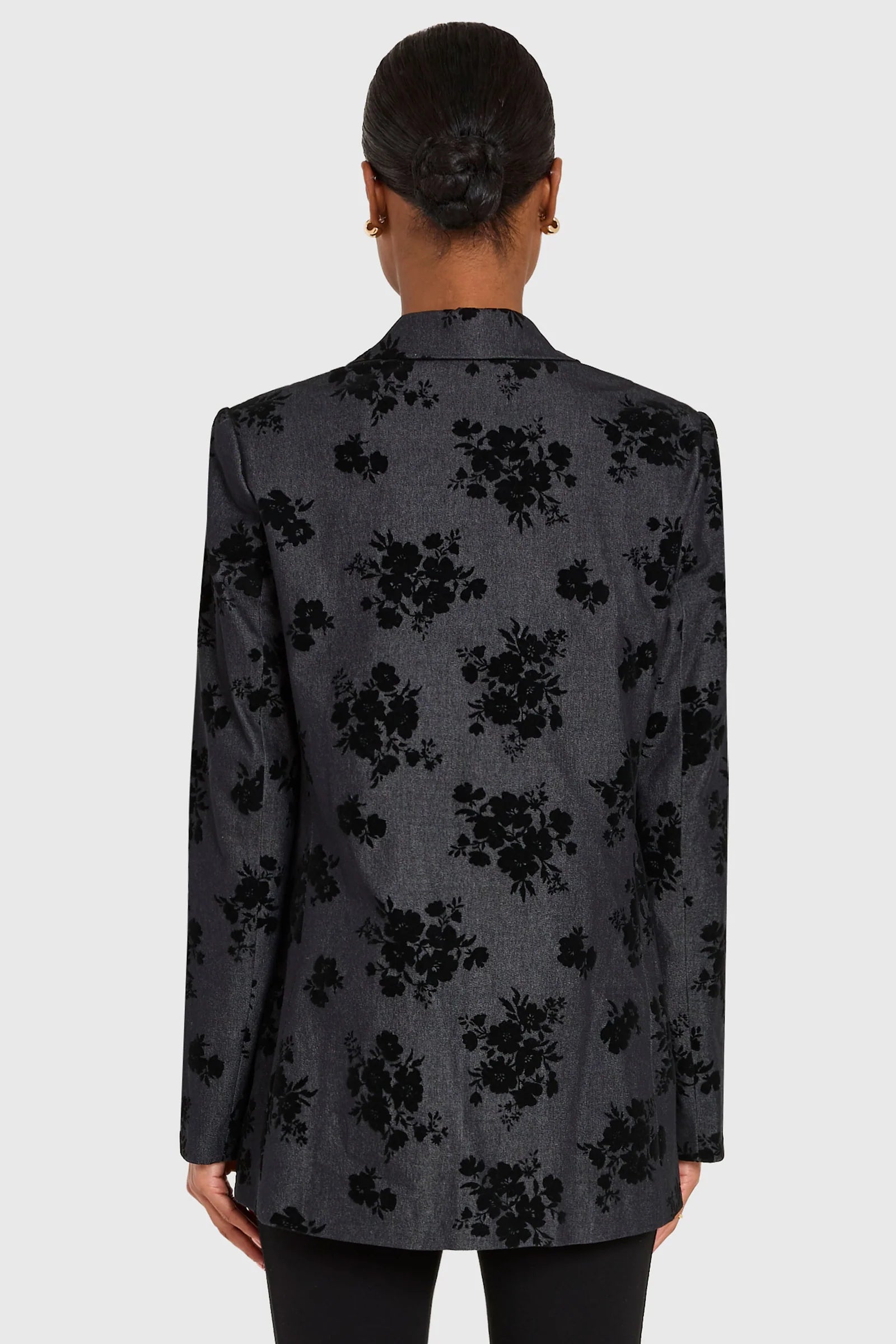 Person wearing a black floral patterned blazer on a white background, back