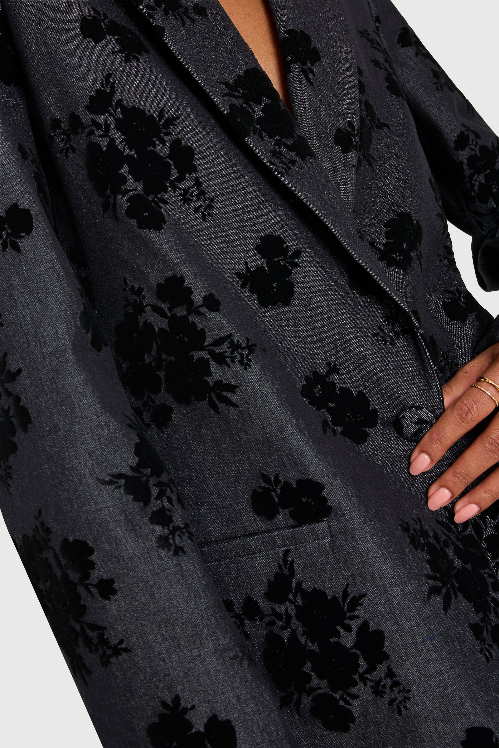 Dark gray blazer with black floral pattern worn by a person, on a light gray background, close up
