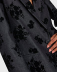 Dark gray blazer with black floral pattern worn by a person, on a light gray background, close up