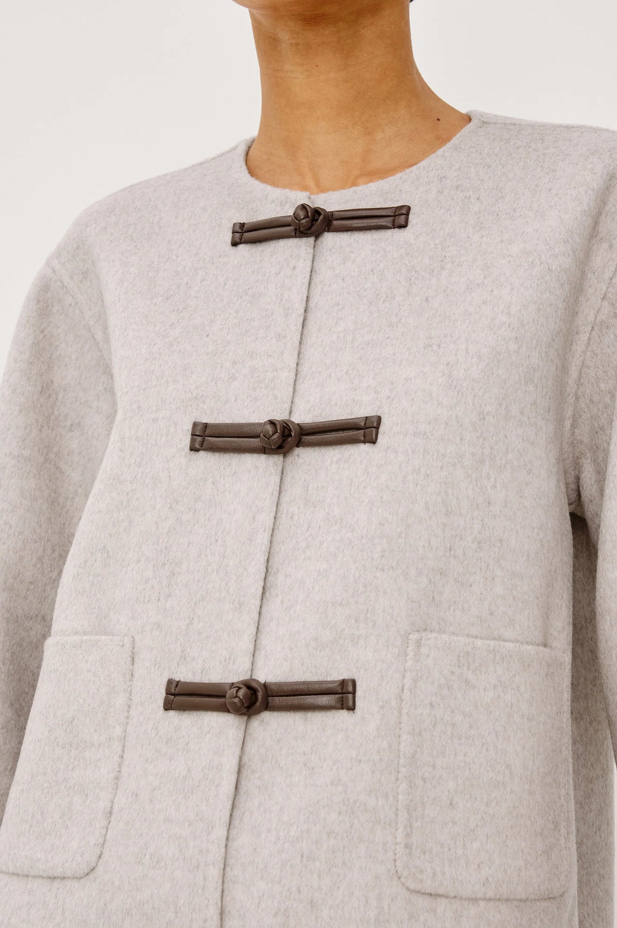model wearing an oat colored jacket with toggle closures, close up
