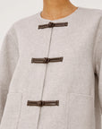 model wearing an oat colored jacket with toggle closures, close up