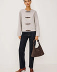 model wearing an oat colored jacket with toggle closures and jeans on a light grey background