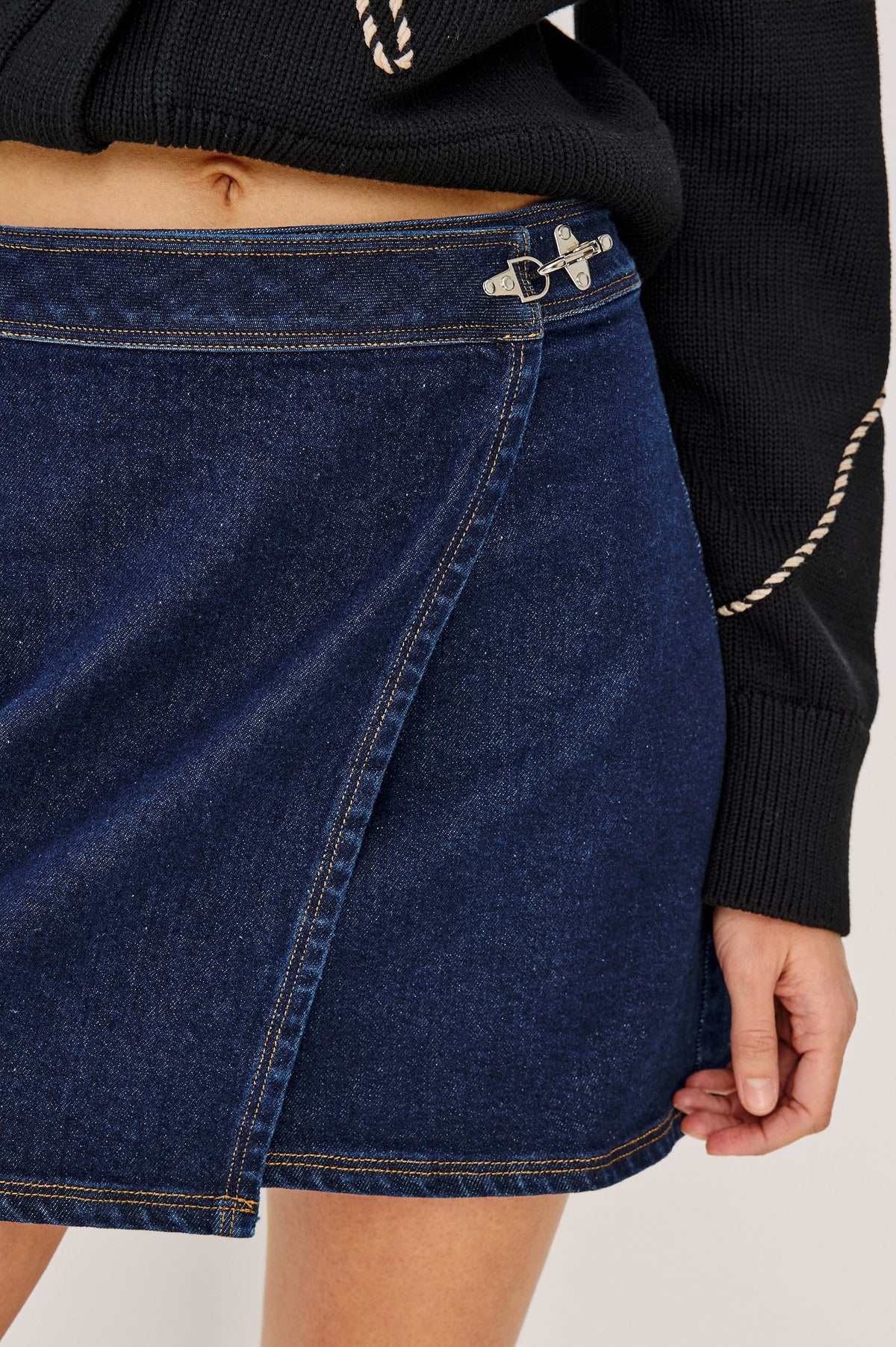 Close-up of a person wearing a blue denim skirt with a black sweater.