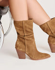 light brown suede boots on a model sitting with a white background