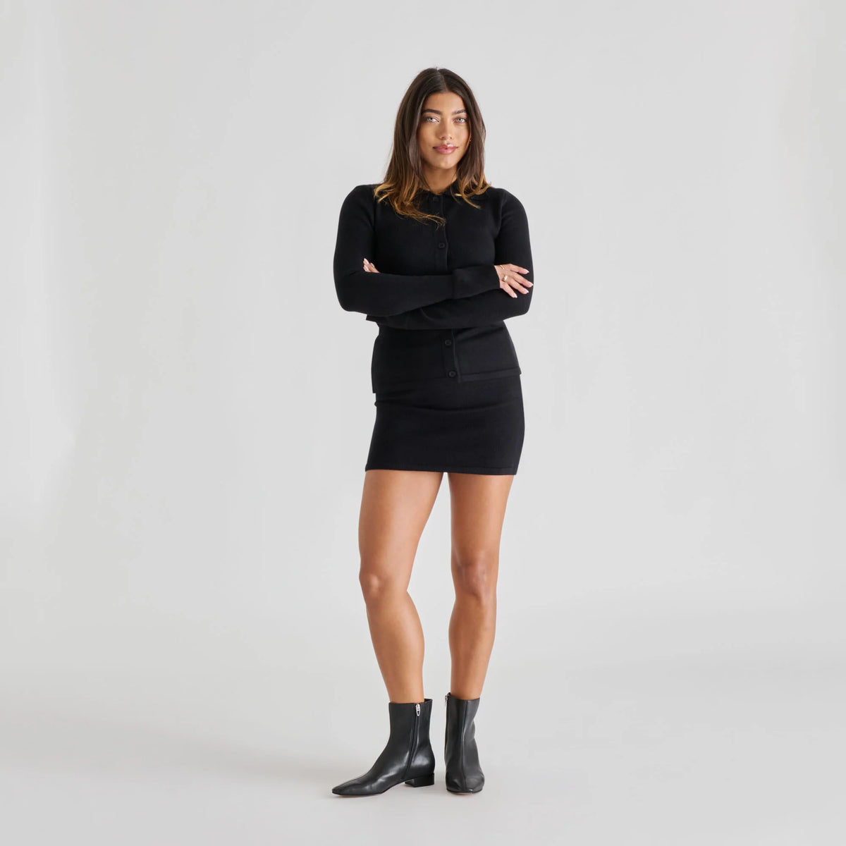 Woman wearing a black outfit with a sweater and skirt on a white background