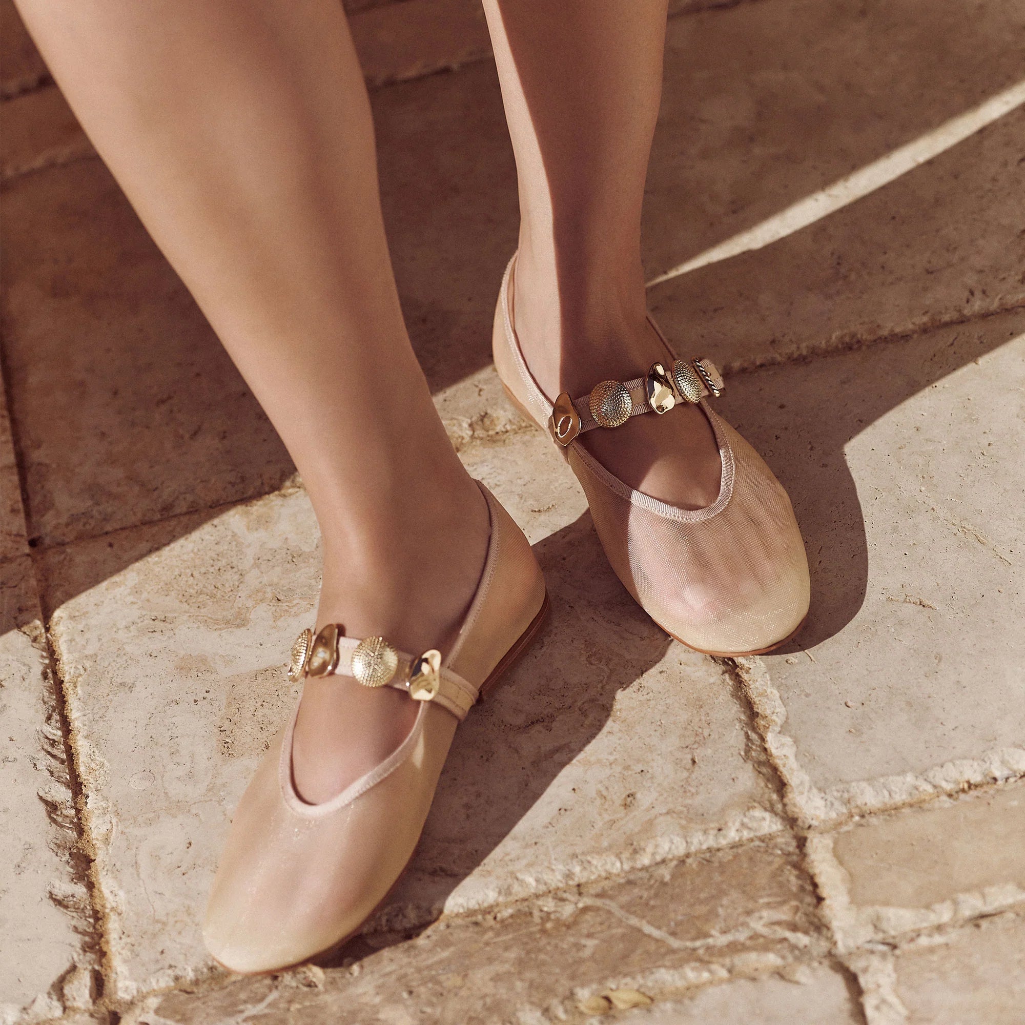 Beige flat shoes with gold buckles on a stone pavement