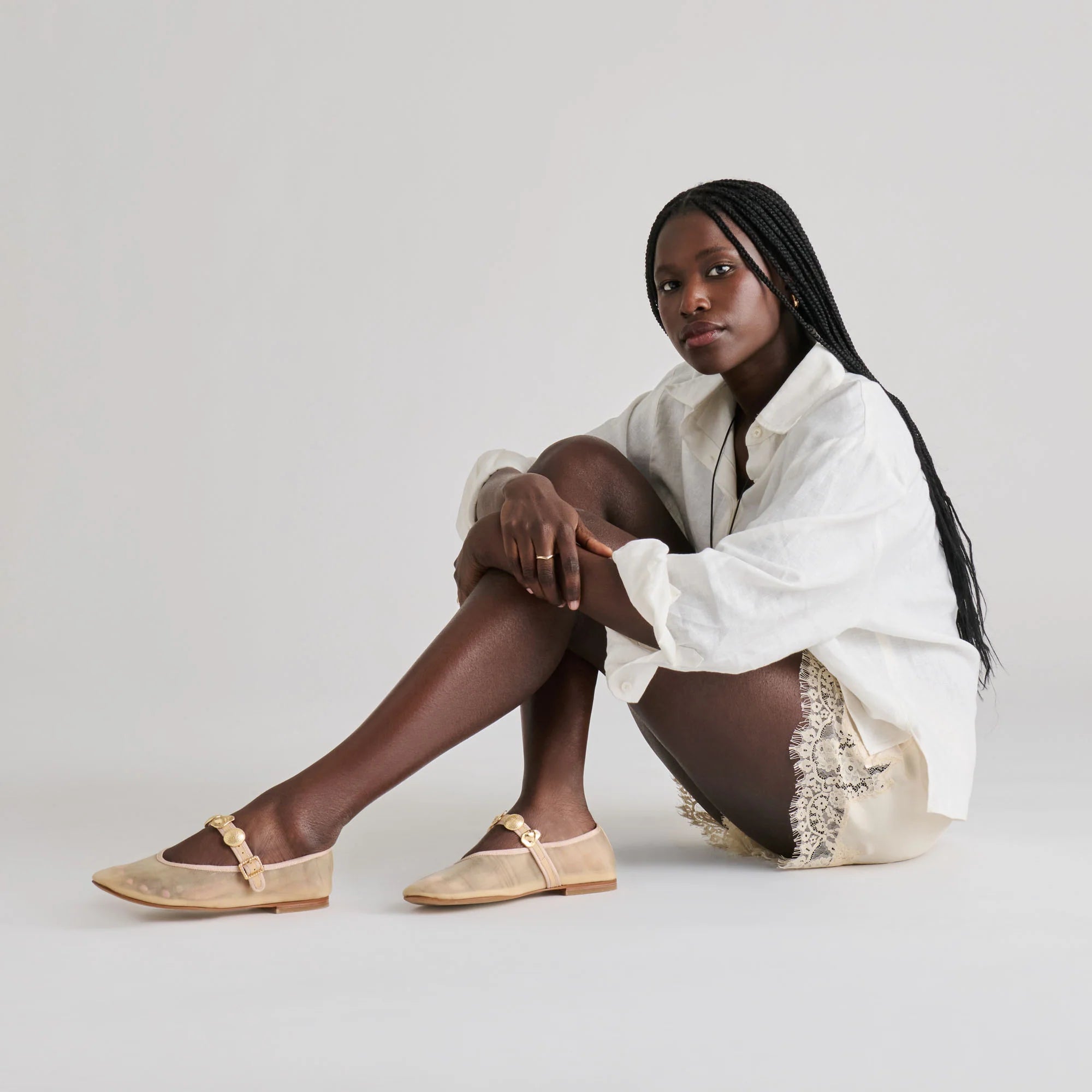 Woman wearing a white shirt and beige sandals sitting on a light gray background