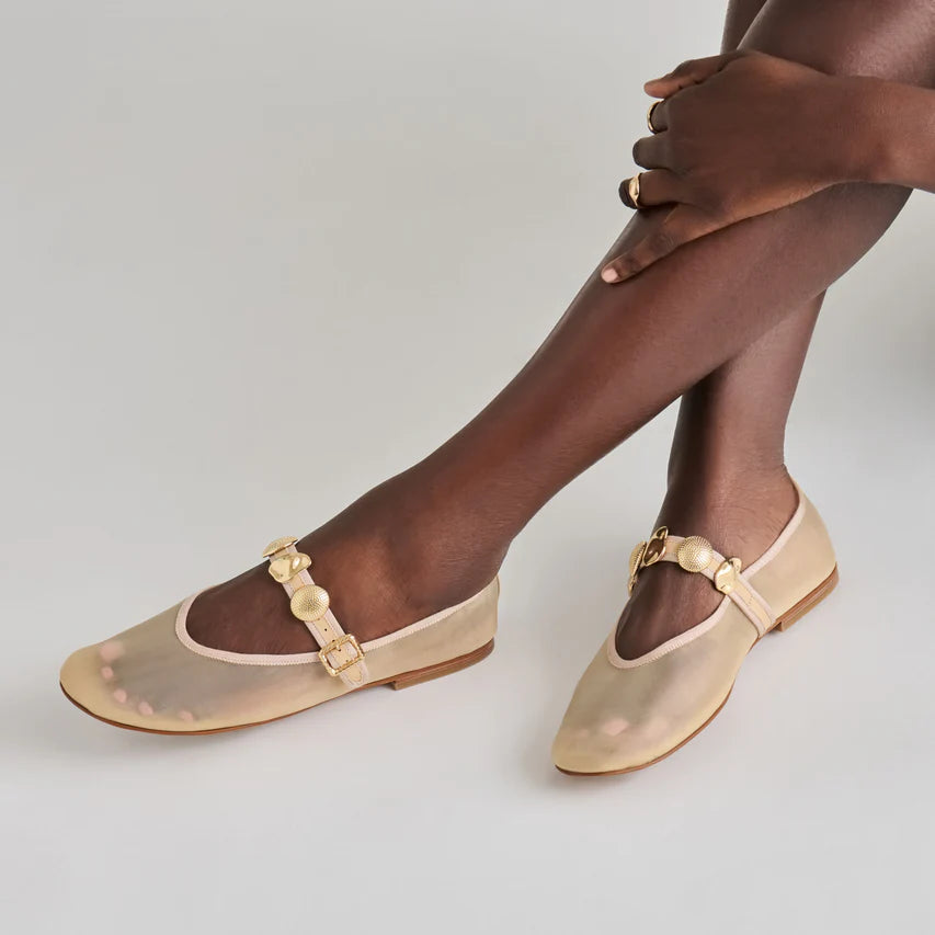 Beige flat sandals with gold accents worn by a person on a neutral background