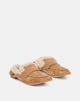A pair of tan suede slip-on loafers with fluffy cream shearling lining, displayed on a clean light gray background.