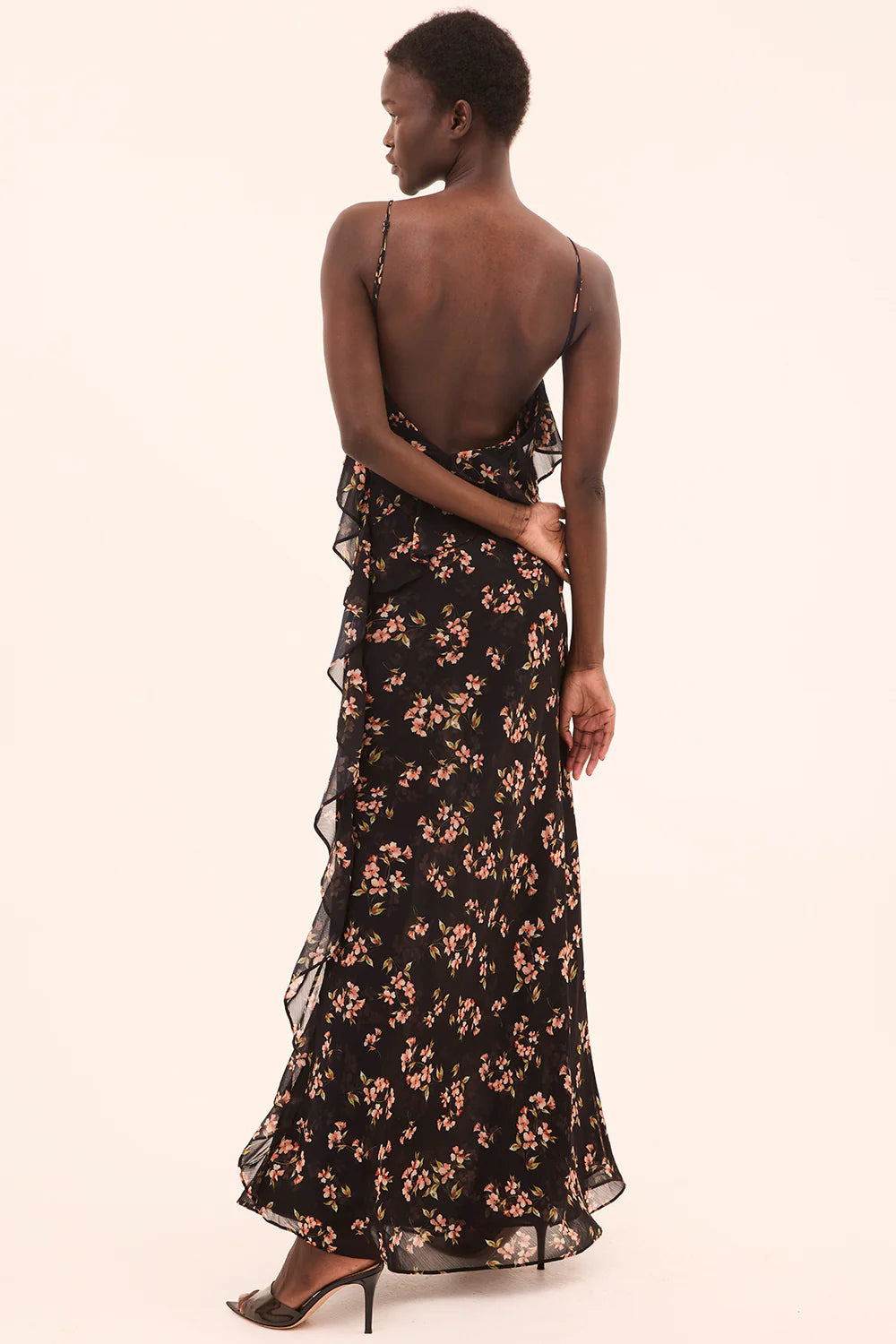 Woman wearing a black floral dress with a plain background, back view
