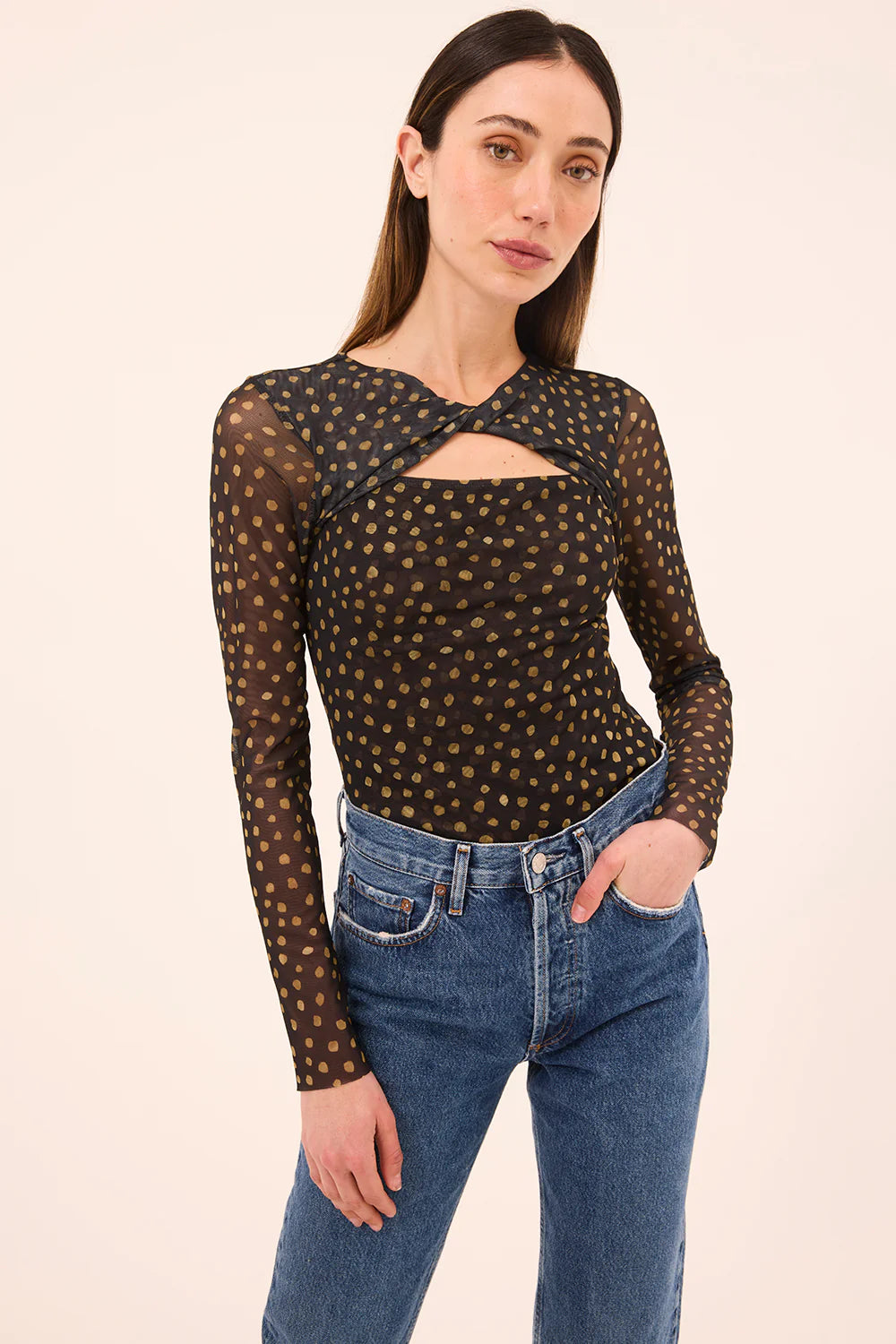 Woman wearing a black mesh top with gold polka dots and blue jeans on a beige background