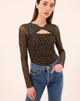 Woman wearing a black mesh top with gold polka dots and blue jeans on a beige background