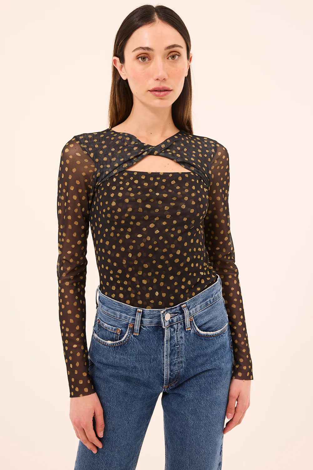 Woman wearing a black sheer top with gold polka dots and blue jeans on a beige background