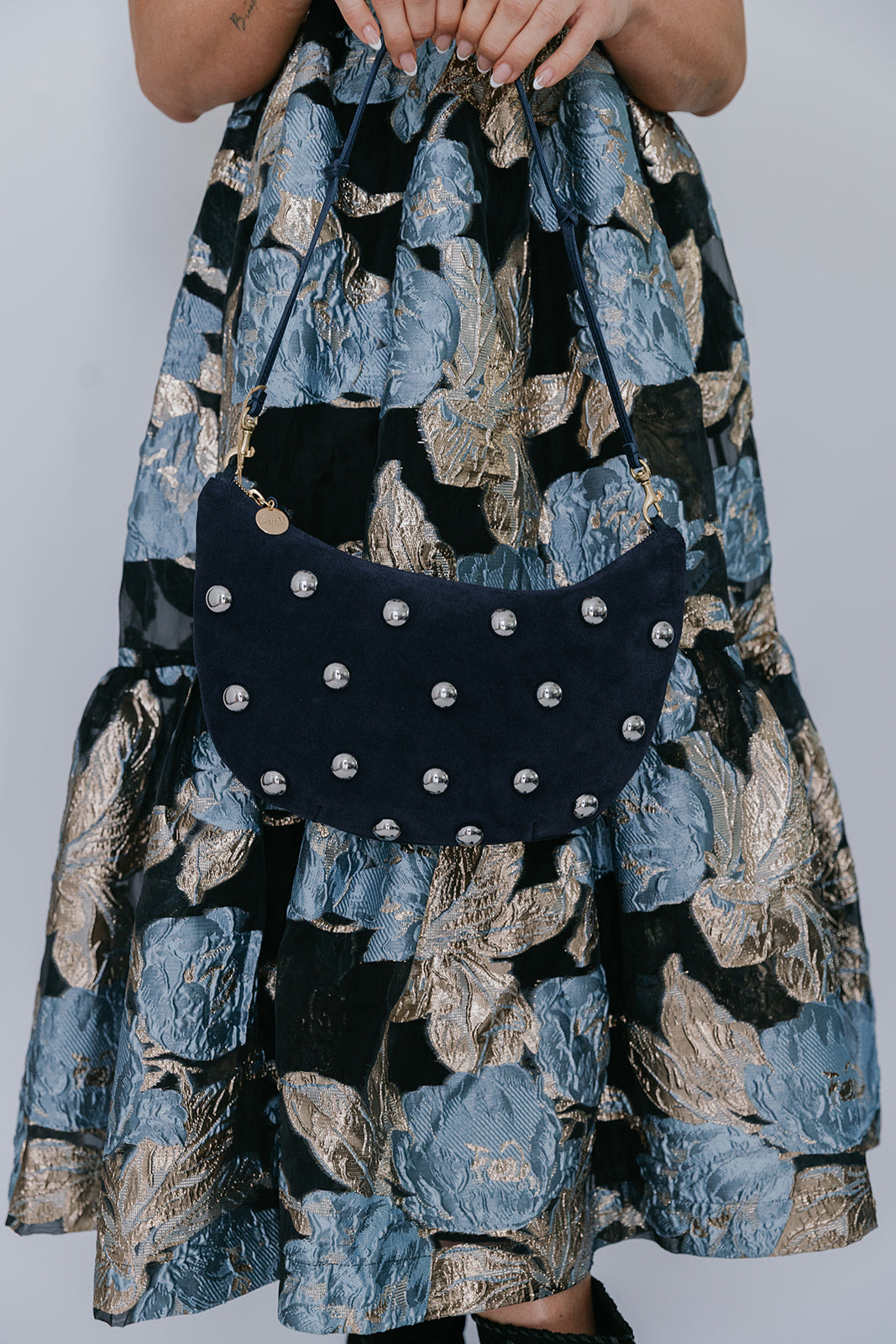 Person wearing a floral dress holding a navy studded handbag against a plain background