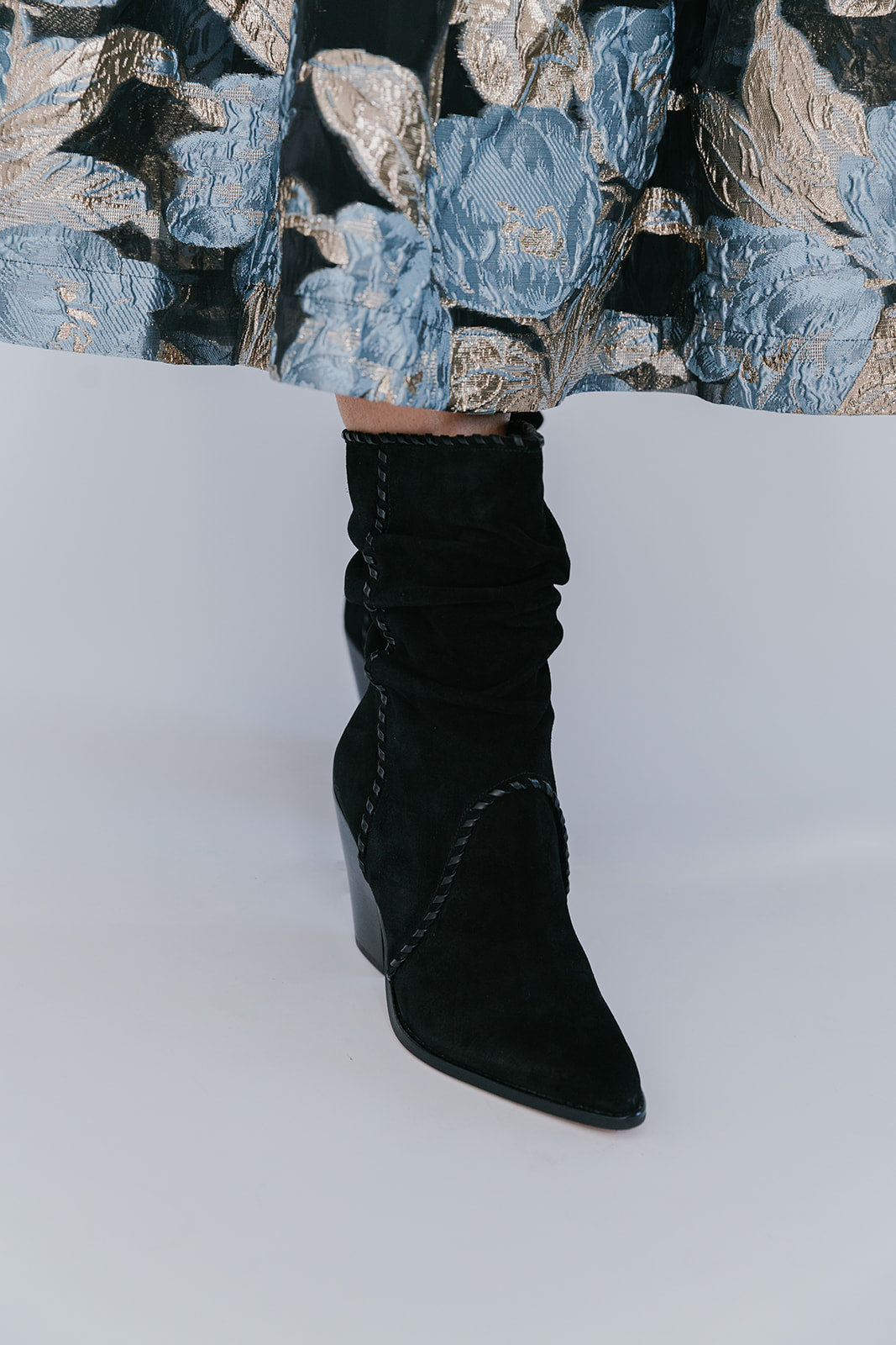 Black knee-high boots worn with a patterned skirt on a white background