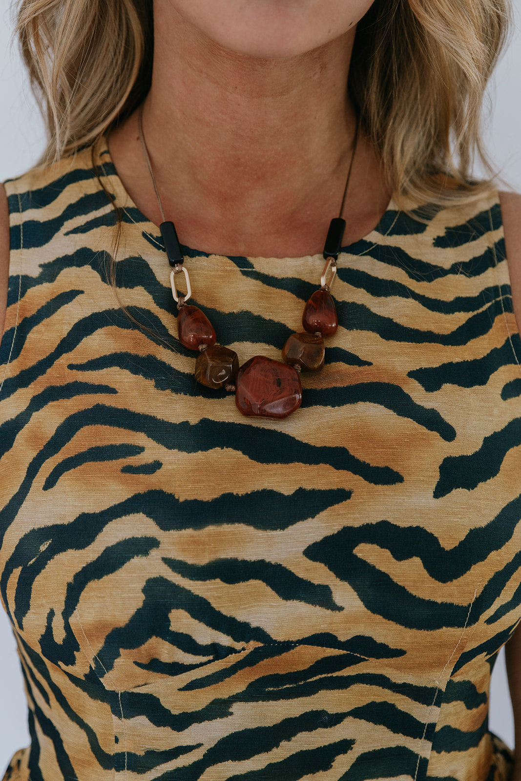 Person wearing a tiger-striped dress with a necklace featuring brown beads.