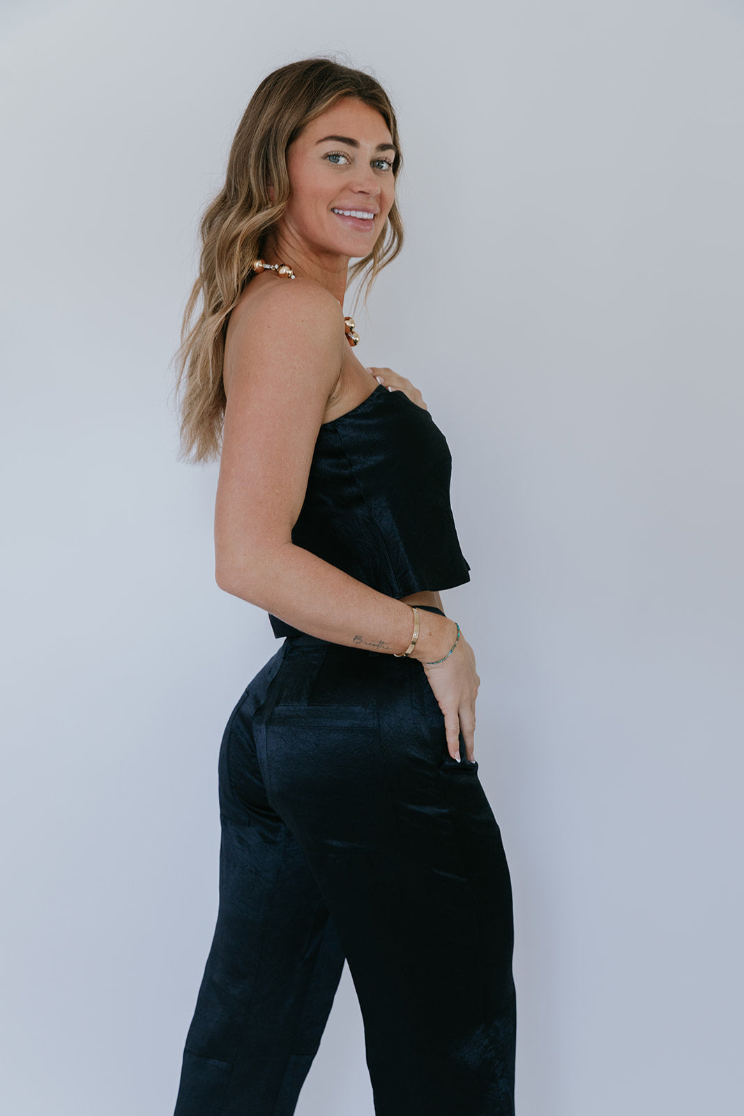 Woman wearing a black satin outfit against a plain background, side close up