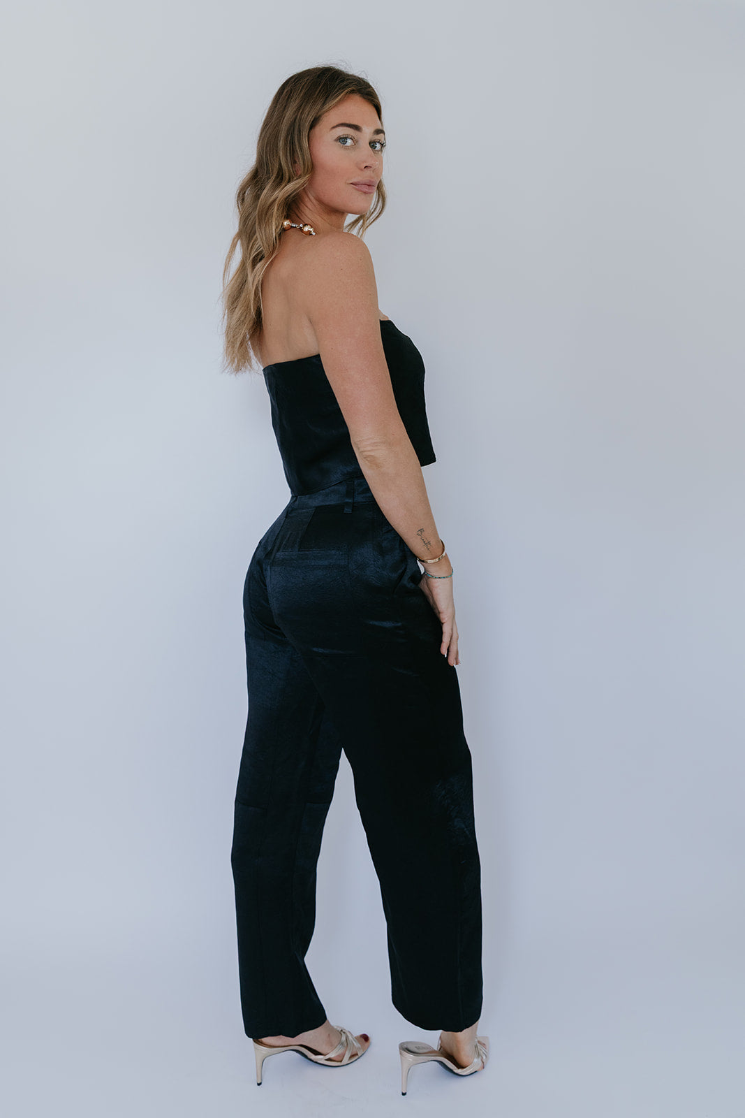 Woman wearing a black strapless top and high-waisted pants against a plain background, back view