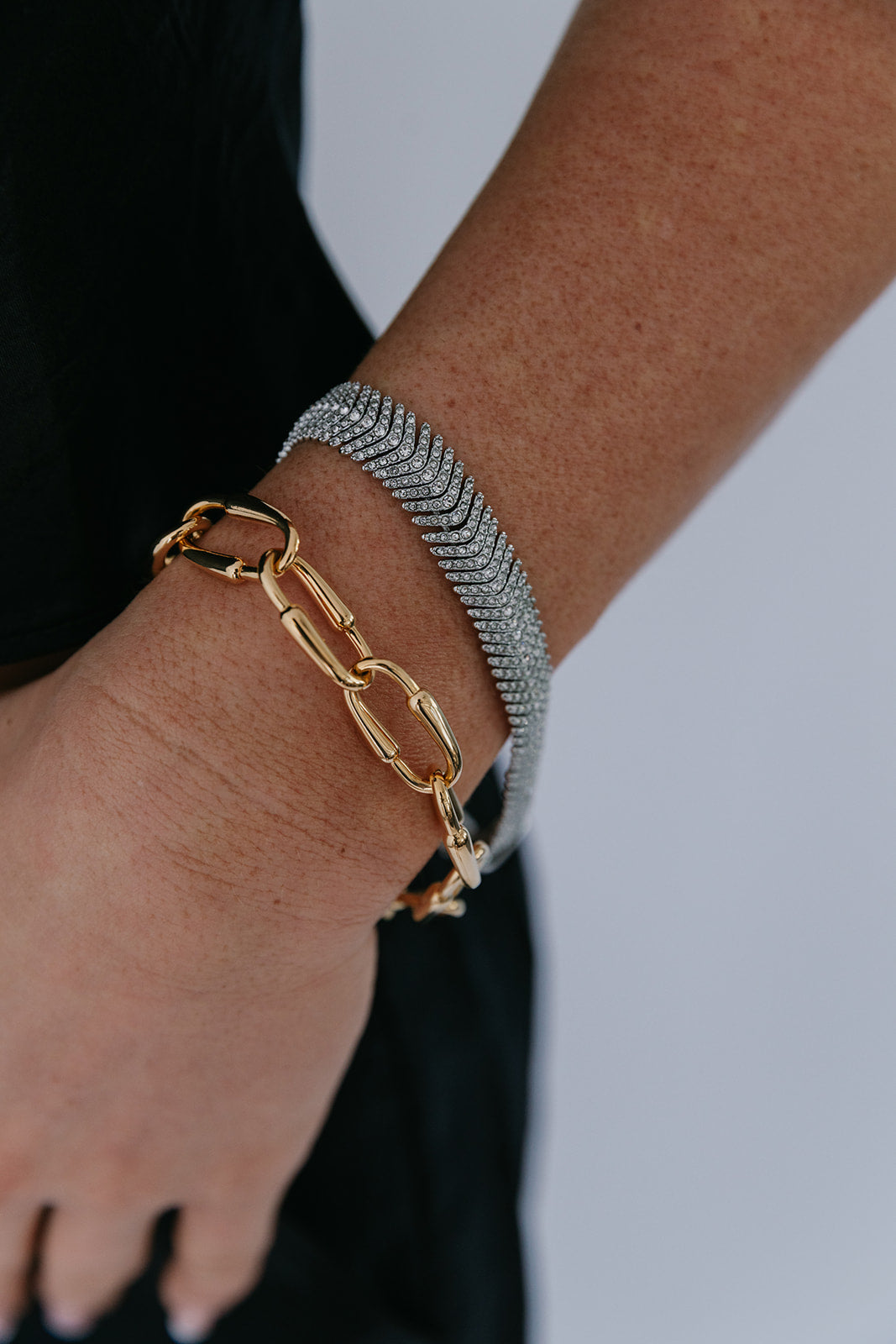 Gold and silver chain bracelets on a wrist against a neutral background