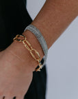 Gold and silver chain bracelets on a wrist against a neutral background