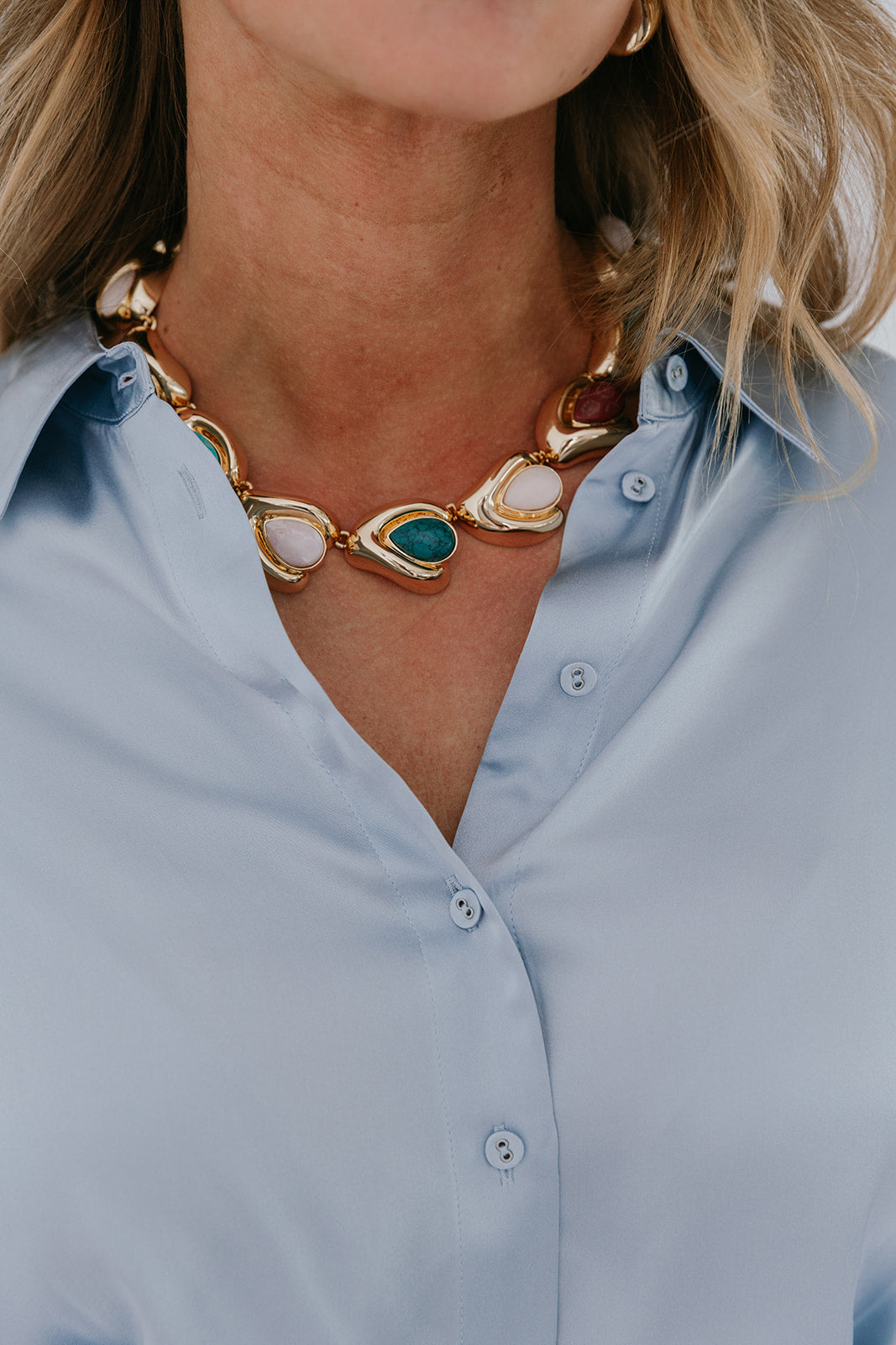 Necklace with gold and gemstone details worn by a person in a light blue shirt.