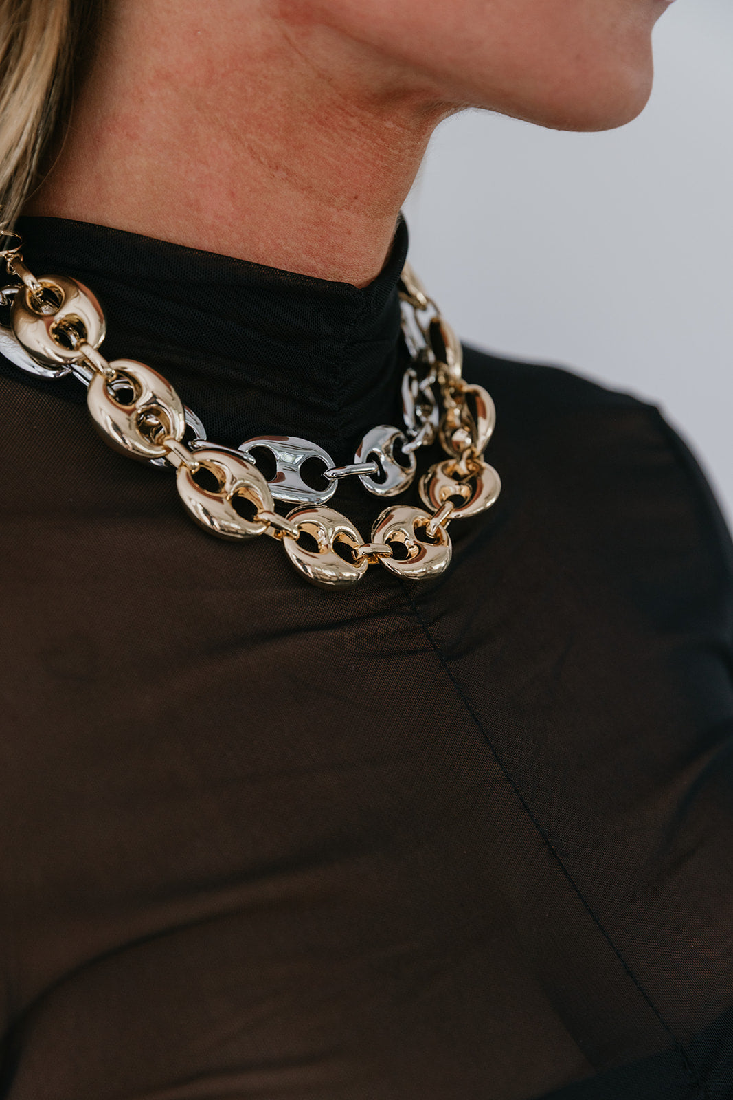 Close-up of a person wearing a gold and silver chain necklace against a neutral background