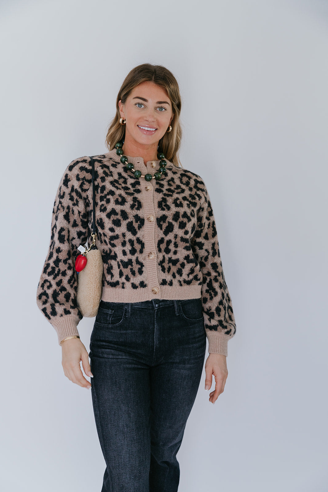 model wearing the leopard windsor cardigan with jeans and a shearling bag with a heart fob on a white background, front