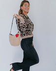 model in a leopard sweater and jeans holding a shearling bag with a heart fob