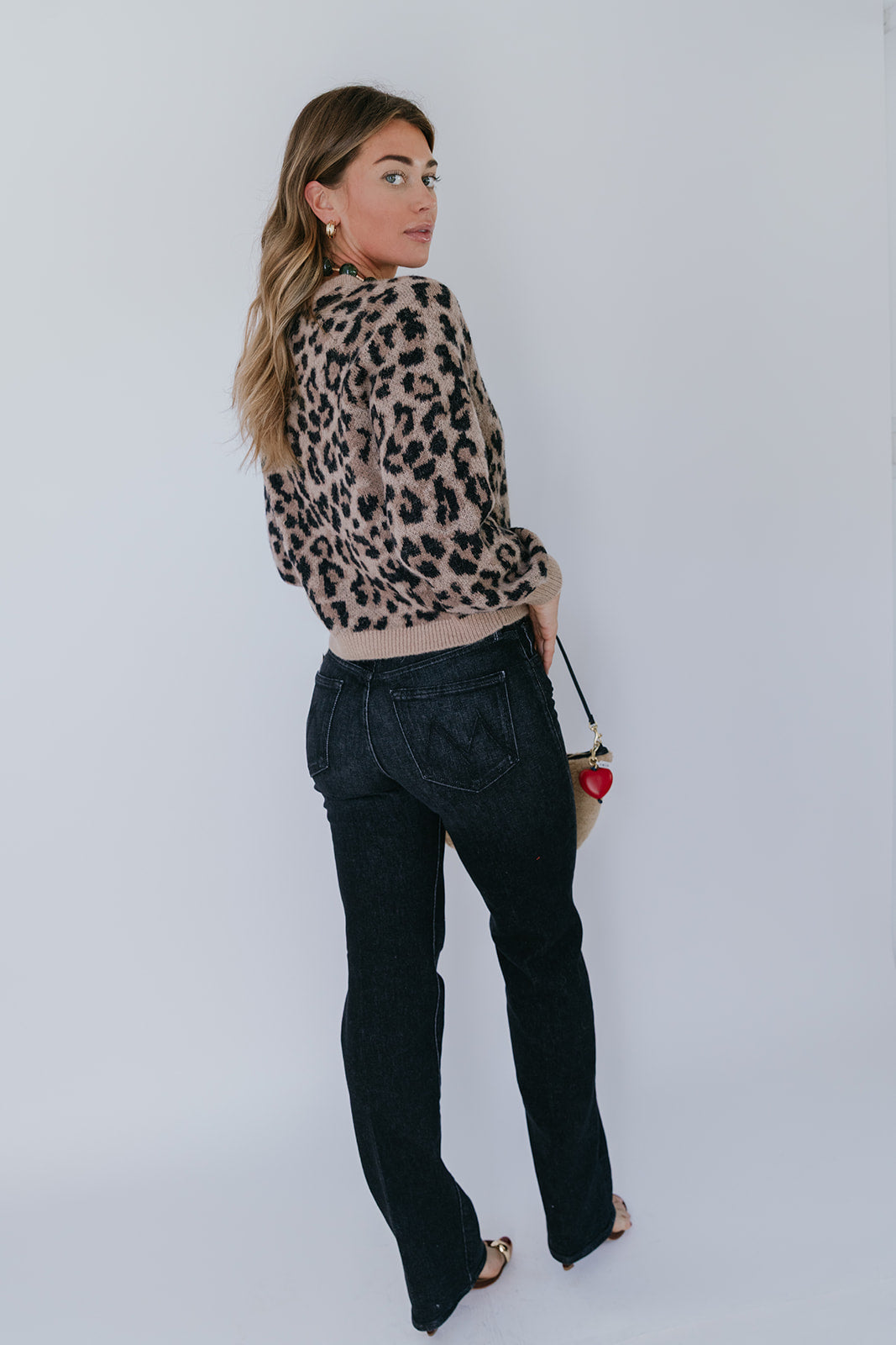 model wearing the leopard windsor cardigan with jeans and a shearling bag with a heart fob on a white background, back