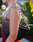 Person holding a black handbag with a checkered strap in an outdoor setting