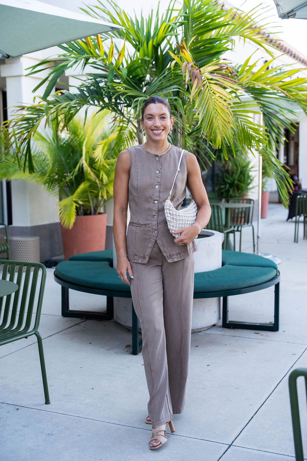 Woman in a beige outfit standing on a patio with plants and furniture.