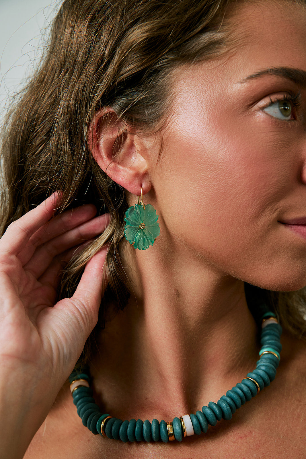 Woman wearing a green floral earring and turquoise beaded necklace.