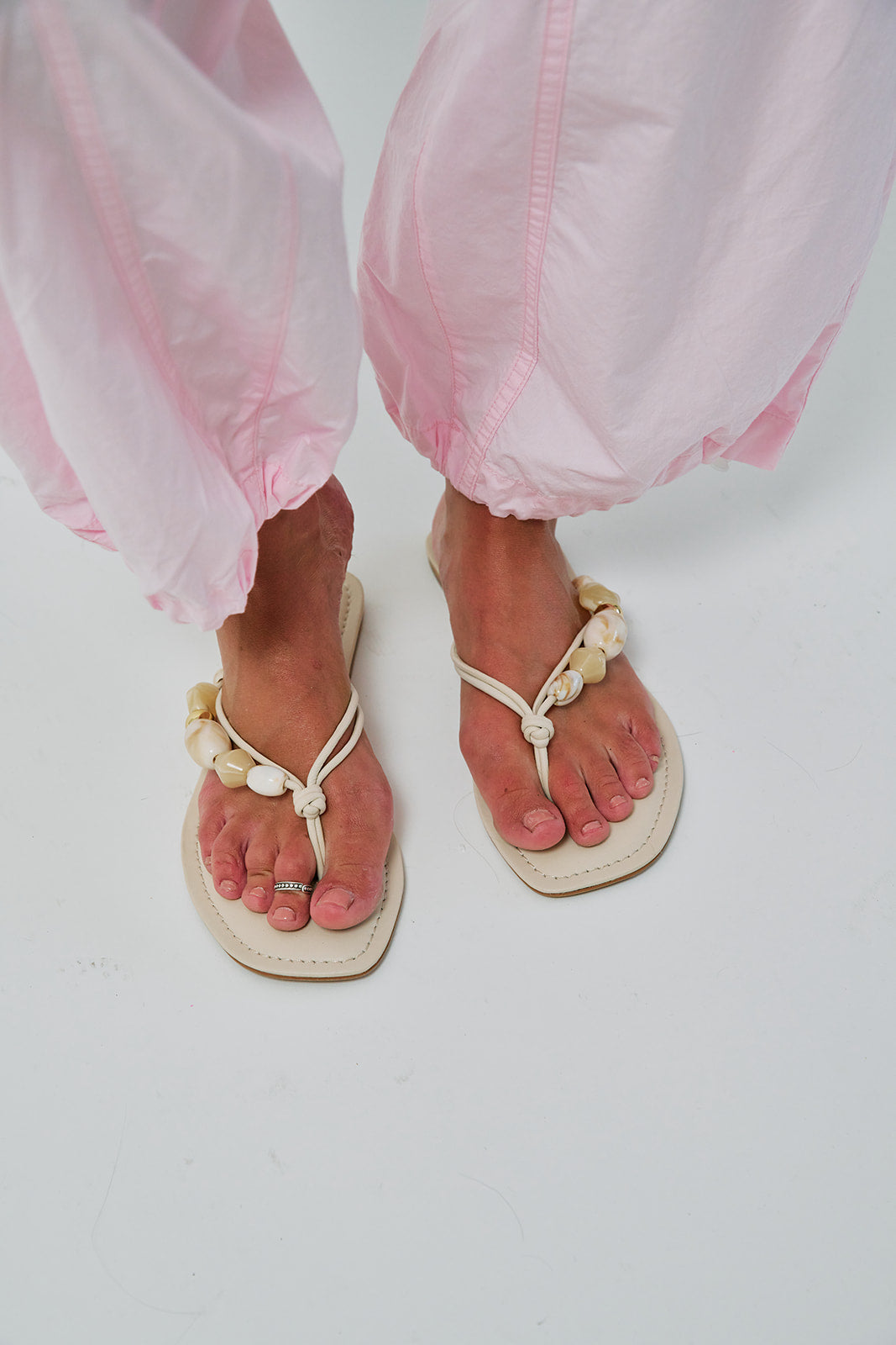 White sandals with decorative elements worn with pink pants on a white background