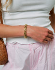 Person wearing a gold bracelet with a white top and pink pants.