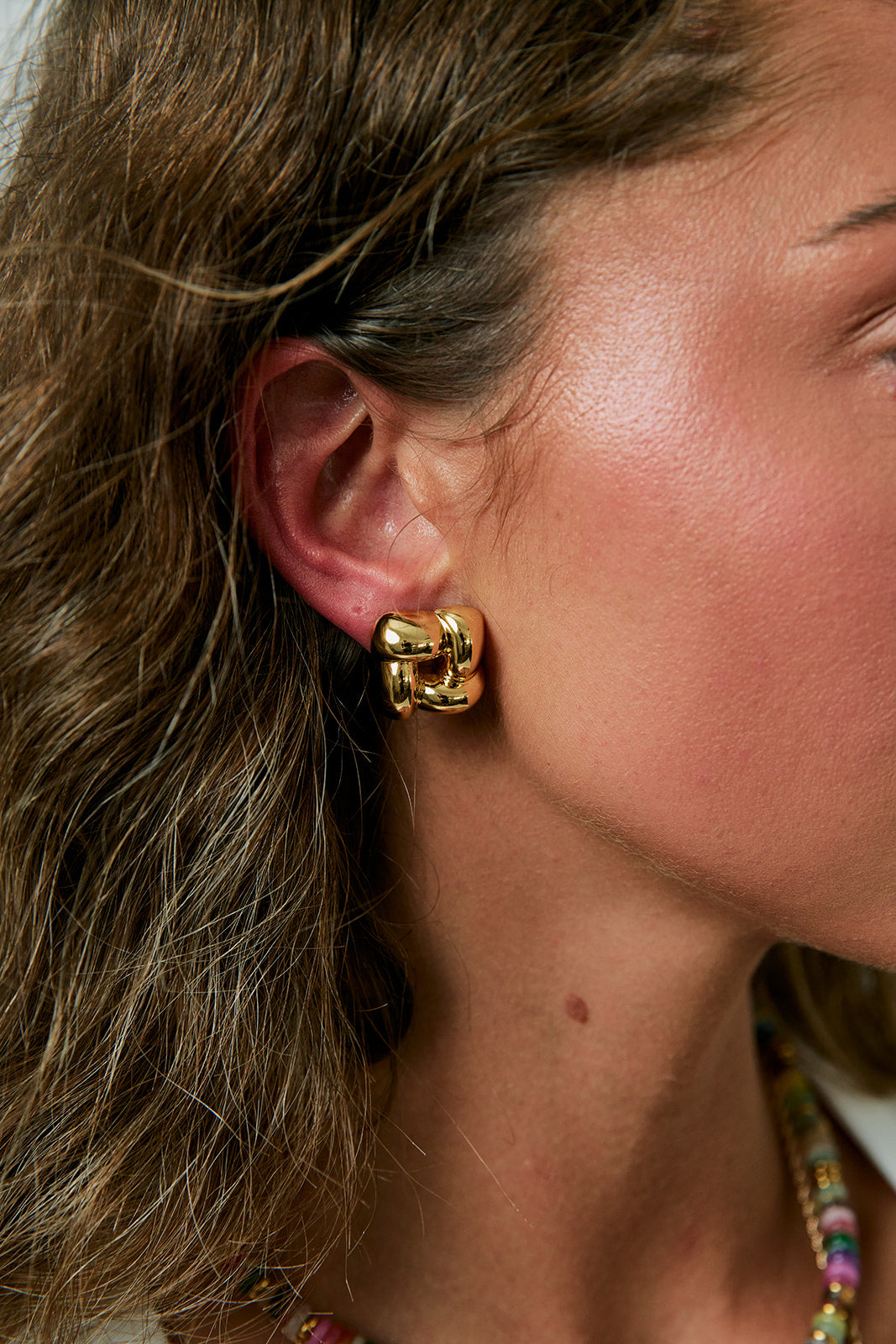 Close-up of a person wearing square  gold earrings with a blurred background