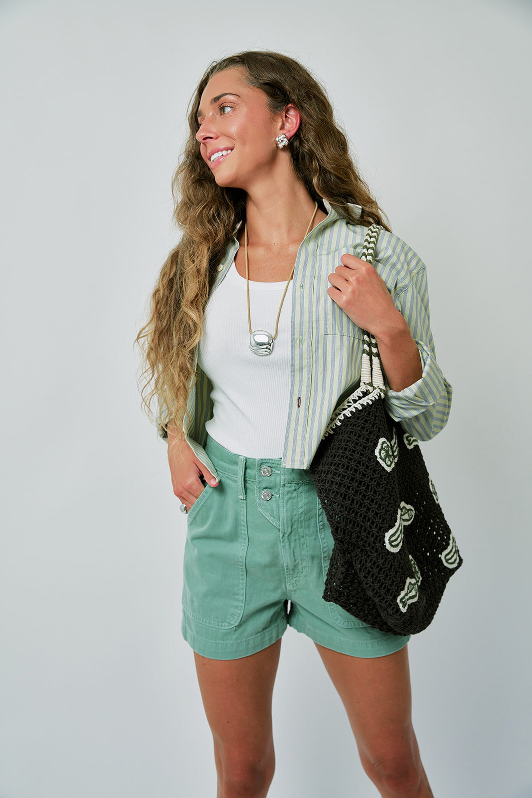 Woman wearing a green striped shirt, white top, and green shorts, holding a black bag with white patterns.