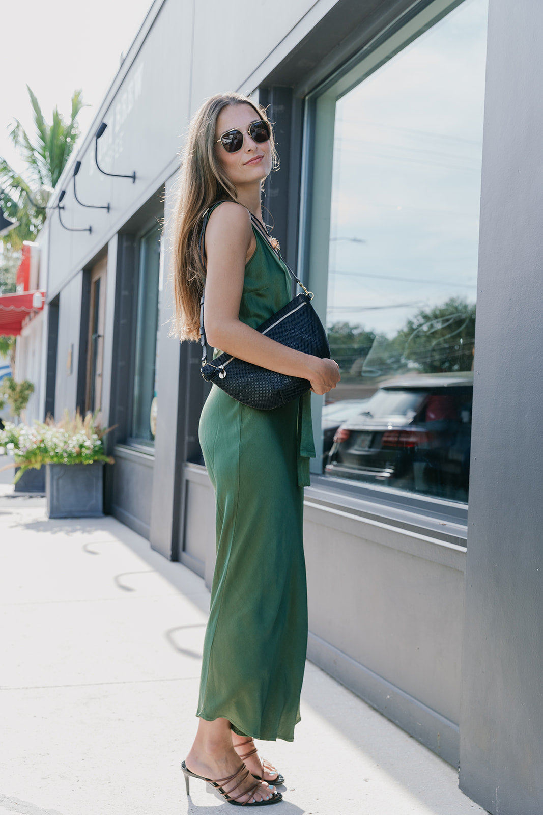 Woman in a green dress standing outside a building with large windows with black perforated grande fanny