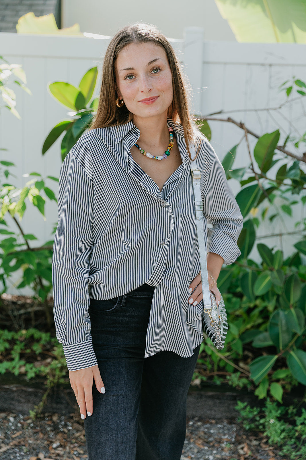 Woman wearing Aris Shirt in Solene Stripe  black pants standing outdoors with greenery in the background front view